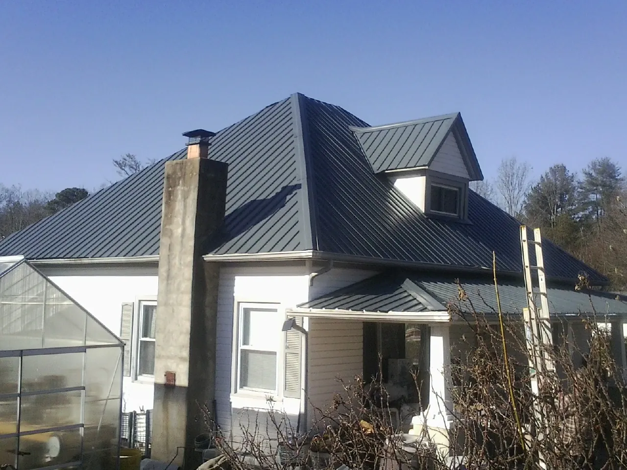 Dark blue standing seam metal roof on a white farmhouse with dormer — Slate & Tile Roof Repair by Roofing Brothers in West Olive
