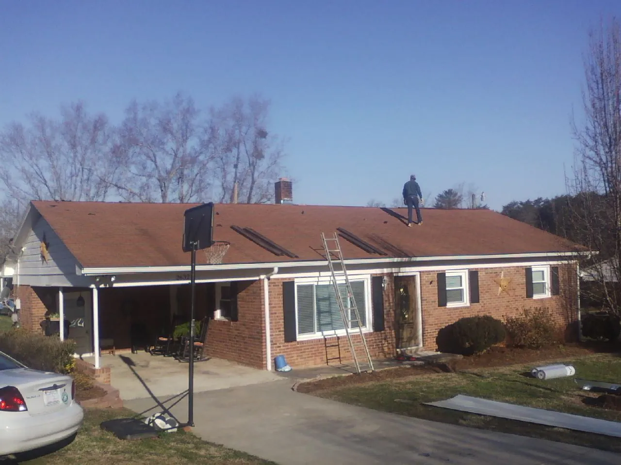 Roofer stripping a shingle roof on a brick ranch before metal panels in West Olive