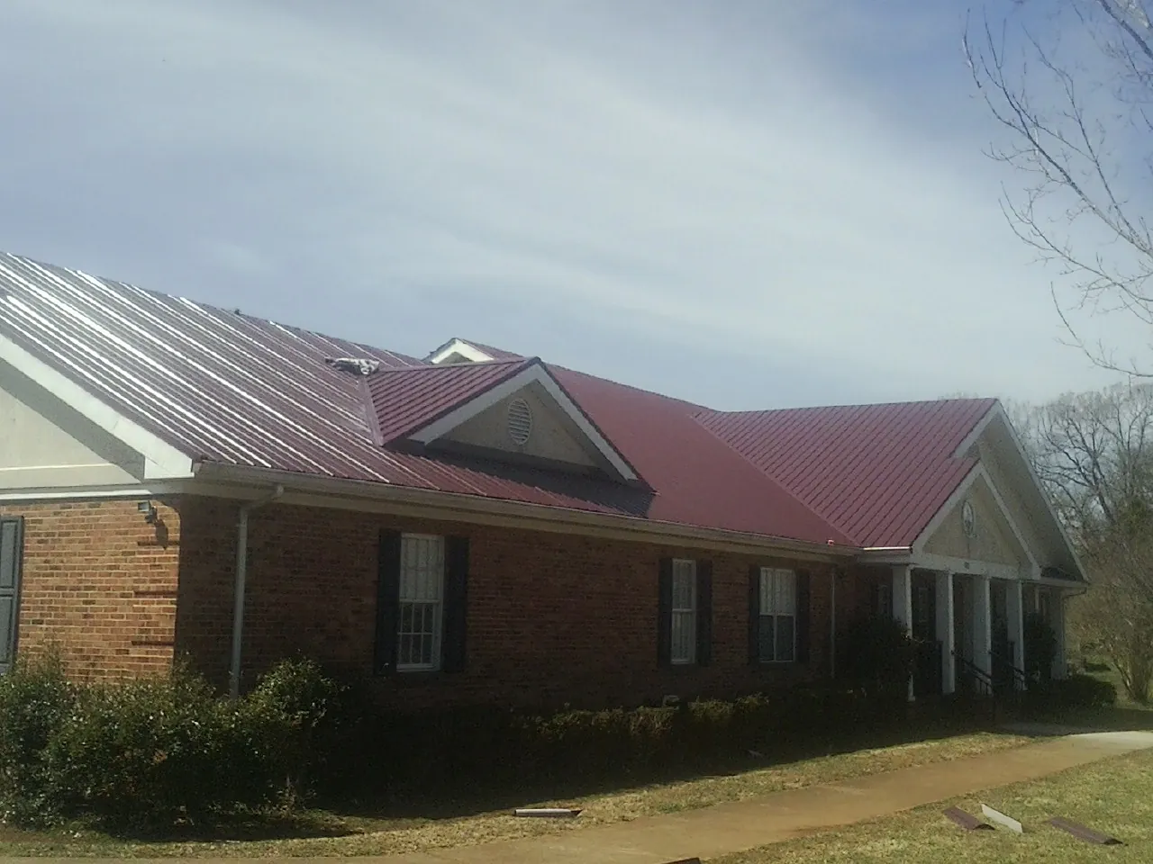 Red metal roof with gabled entries on a long brick building, from a Hail Damage Roof Repair job in West Olive