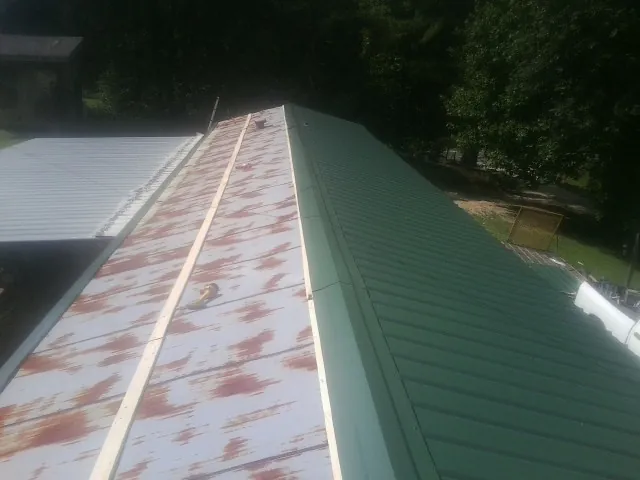 Old rusted panels beside newly installed green metal roofing — Wind Damage Roof Repair by Roofing Brothers in West Olive
