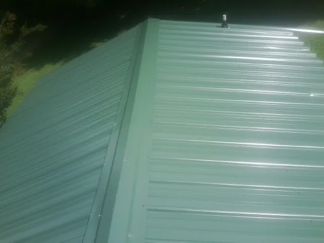 New green metal panels meeting at the ridge of a roof — Flat Roof Repair work by our crew in West Olive