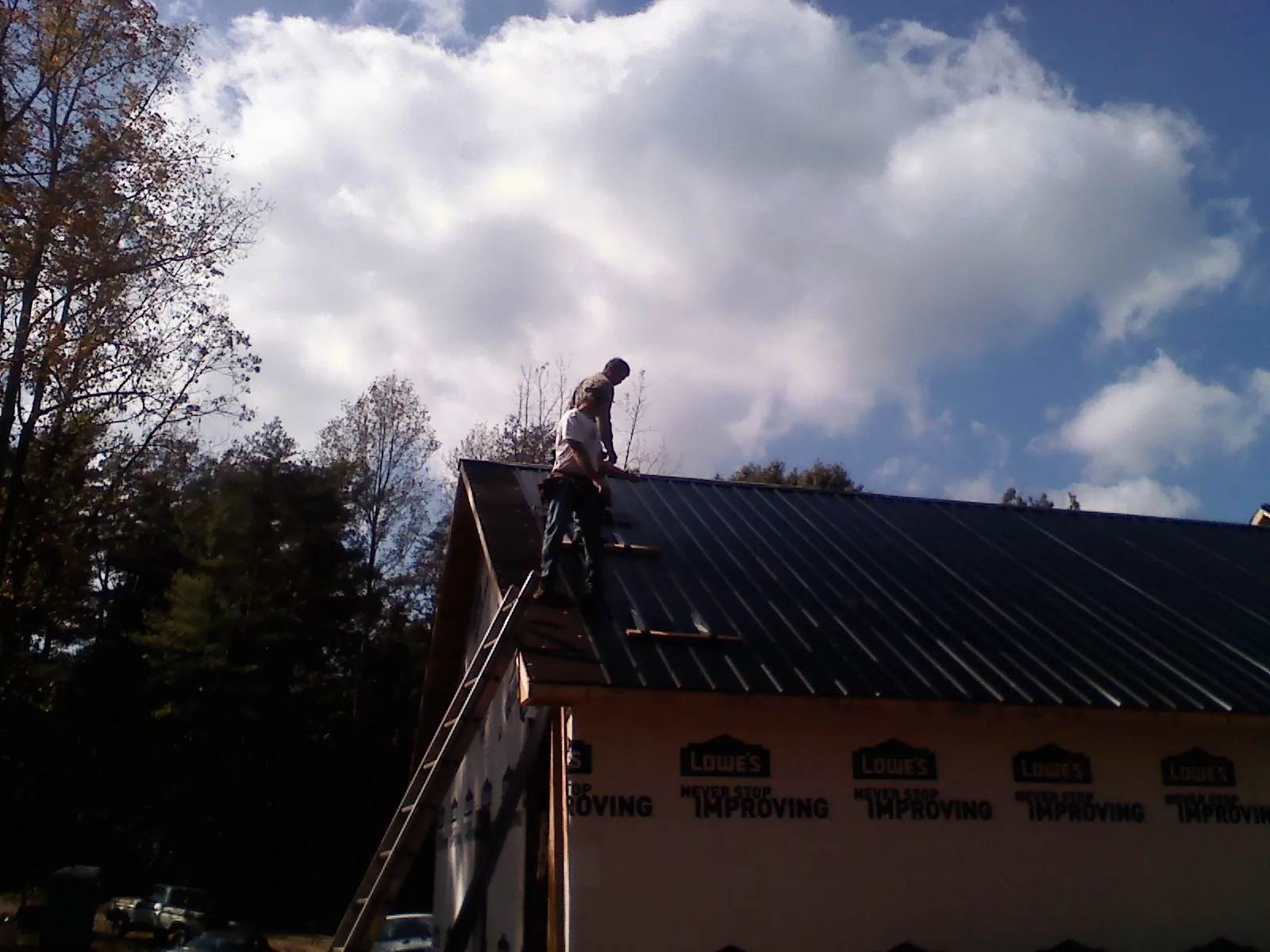Roofer fastening dark metal panels high against a cloudy sky, from a Roof Inspection job in West Olive