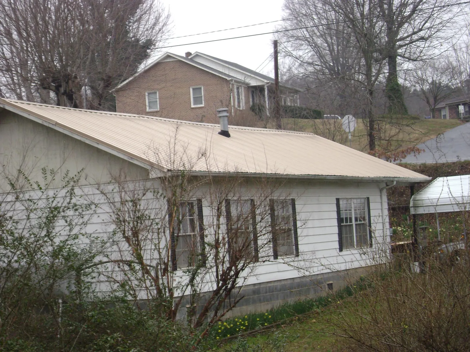 Tan metal roof on a white sided house set into a hillside — Commercial Roofing by Roofing Brothers in West Olive