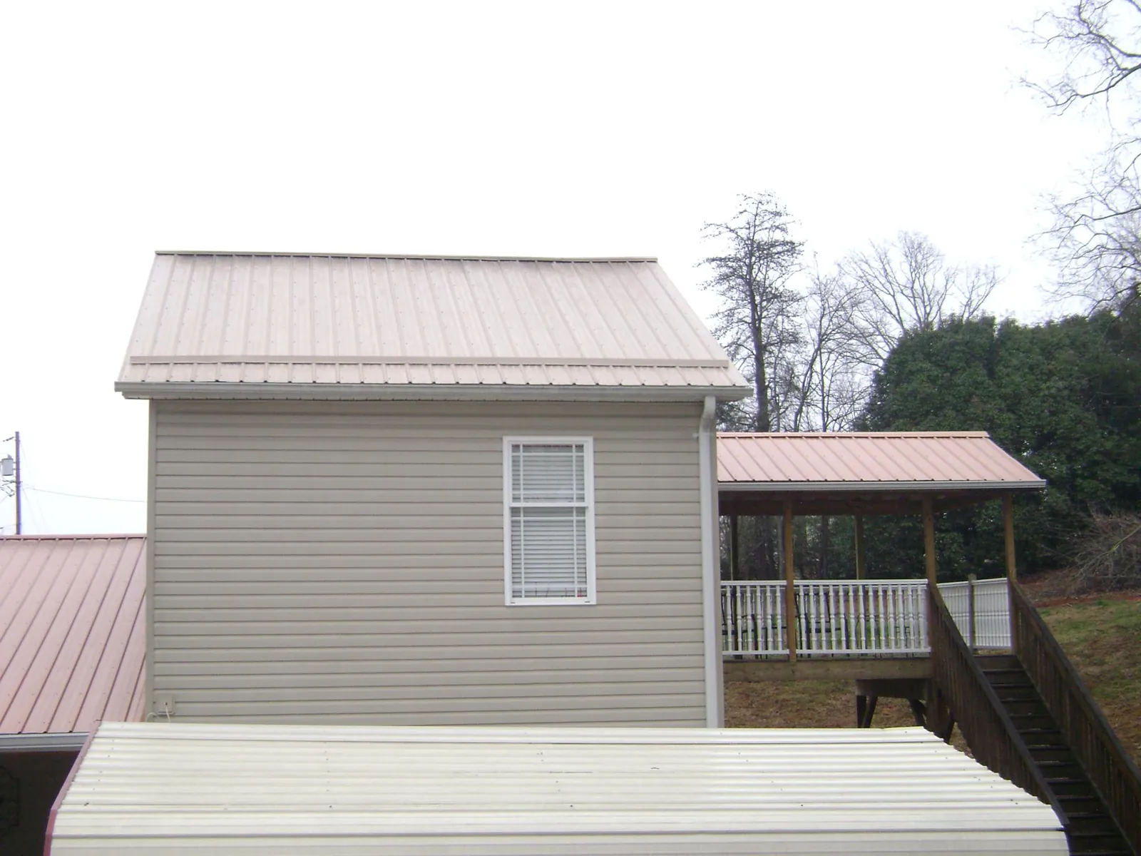 Tan metal roofs on a two story addition and attached porch, from a Roof Replacement job in West Olive